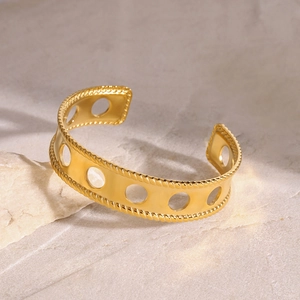 Close-up of golden hollow cuff bracelet with circular patterns and twisted rope edge detail