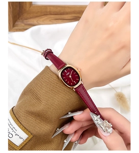 Gros plan d'une montre en cuir bordeaux avec boîtier ovale en or rose au poignet d'une femme