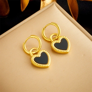 Detail of golden hoop earrings with black heart charms and textured wavy edges