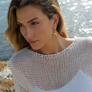 Boucles d'oreilles étoiles de mer en acier doré 18K portées par un mannequin à la mer
