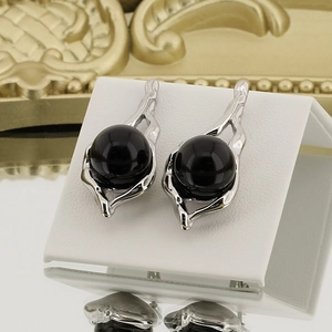 Detailed shot of silver stainless steel earrings with large round black pearls on white stand