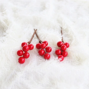Close-up of three faux red berry stems with glossy beads on white faux fur background