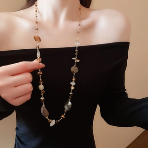 Dettaglio della collana di perle con cristalli marroni su un abito nero sobrio