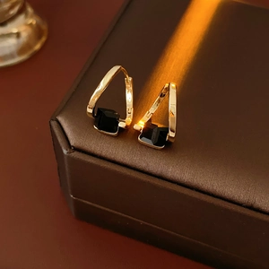 Close-up of golden geometric V-shaped earrings with square black gemstone on leather