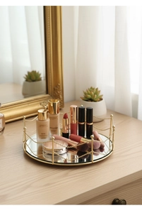 Detail view of round gold mirrored tray holding cosmetics on a wooden tabletop