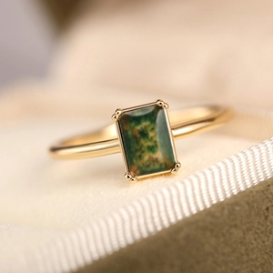 Macro detail of a gold ring featuring a rectangular moss agate stone with four-prong setting