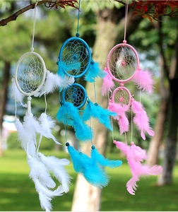 Three colorful handmade dreamcatchers with feathers hanging on a tree branch outdoors