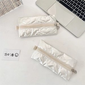 Close-up of white quilted PU pencil cases featuring heart and bow patterns on a desk