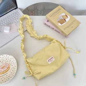 Detailed close-up of yellow pleated canvas bag with colorful wooden beads on white desk