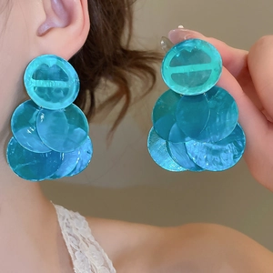 Close-up of green round shell earrings with multi-layered fringe and pearlescent finish
