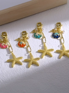 Macro detail of enamel starfish and shell keychains with pearls and gold-plated finish