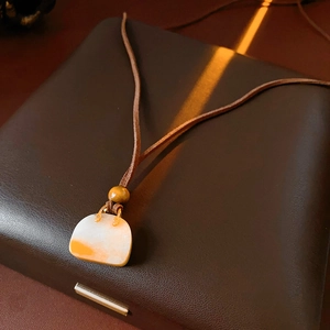 Close-up of bag-shaped resin pendant with brown leather cord and wooden bead detail
