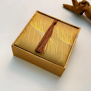 Top view of a square gold brocade jewelry box featuring a stylish brown tassel detail