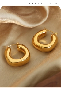 Detailed macro view of U-shaped gold-plated titanium earrings on satin background