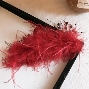 Detail view of a luxury red feather hair claw clip with glass beads and silk accents