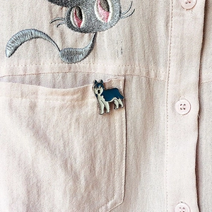 Gros plan d'un pin's husky émaillé bleu et blanc sur la poche d'une chemise rose