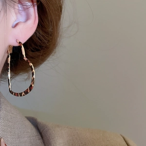Close-up of leopard print heart-shaped hoop earrings worn by a model in soft lighting