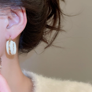 Close-up of elegant white and gold enamel C-shaped hoop earrings on a female model