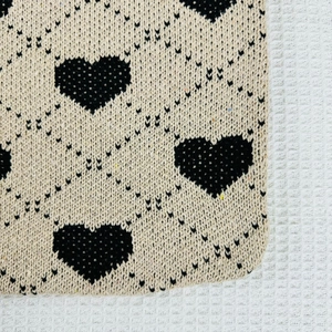 Close-up of beige knit fabric with black heart patterns showing detailed weave texture