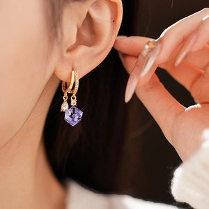 Detail of gold huggie hoop earring featuring a purple cube zircon stone on a female model