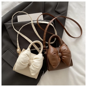 Detail of cute bow-knot handbags in cream and brown PU leather with top handles