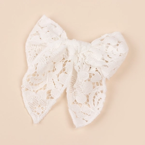 Close-up of white lace bow hair clip featuring delicate floral embroidery on beige background