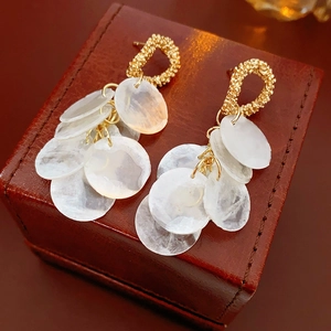 Detail of round golden textured earrings with multi-layered white seashell tassels