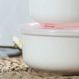 Close-up of stacked white ceramic storage bowls with lids on a woven natural placemat