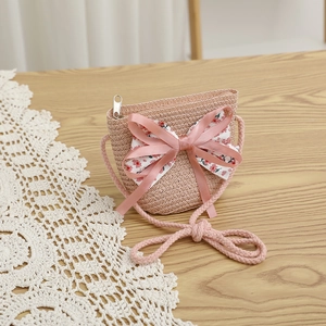 Détail d'un sac bandoulière en paille rose pour fille avec un grand nœud sur fond bois