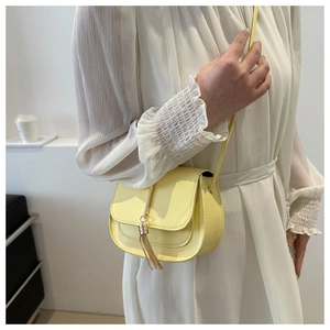 Detail of light yellow saddle bag with fringe tassel and metallic charm on white dress