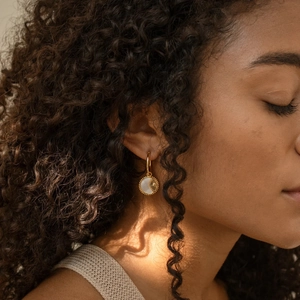 Primer plano de pendientes de oro de 18K con colgante de sol de nácar en modelo