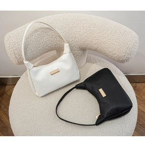 Detail view of black and white leather shoulder bags with gold hardware on a plush chair