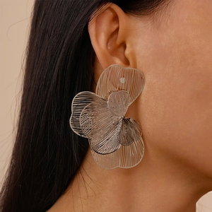 Detailed view of silver hollow flower stud earrings worn on a model with metallic texture