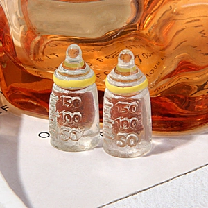 Macro shot of two miniature resin baby bottles with yellow collars and clear volume scales