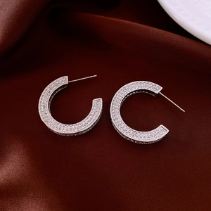 Detail of silver C-hoop earrings with sparkling cubic zirconia on red silk fabric