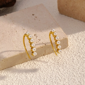 Golden titanium steel hoop earrings with white pearls on a textured stone background