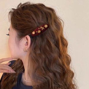 Close-up of red velvet hair clip with gold zodiac charms worn on wavy brown hair
