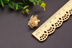Detail shot of a yellow floral pearl earring on black texture beside a wooden ruler