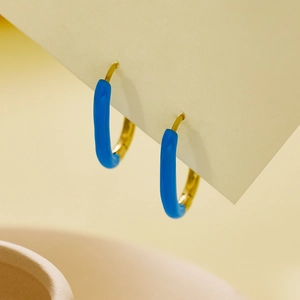 Detail goldener Creolen mit lebhafter blauer Emaille-Beschichtung auf schlichtem Metall