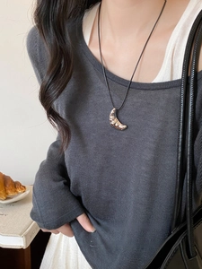 Detail view of croissant shaped silver pendant on black leather cord worn by a model