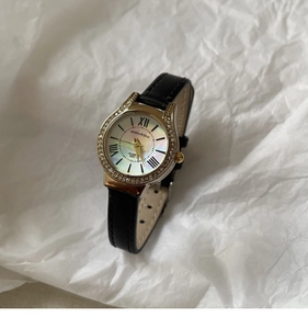 Close-up of gold shell dial watch with crystal bezel and black leather strap