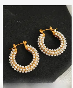 Détail de boucles d'oreilles dorées en C avec perles blanches sur surface gris foncé