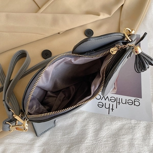 Gray heart-shaped crossbody bag with gold zipper and tassels shown from a top-down view