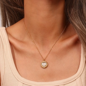 Détail d'un collier doré élégant avec pendentif en forme de cœur et soleil rayonnant
