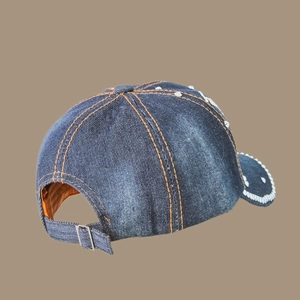 Detail view of dark blue denim baseball cap with orange stitching and white rivet accents