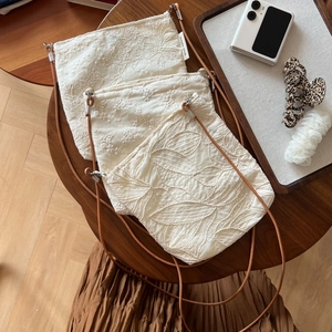 Three beige linen crossbody bags with delicate floral embroidery and leather straps