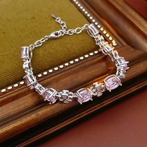 Close-up of a silver-toned bracelet with pink oval zircon and clover detail on green velvet