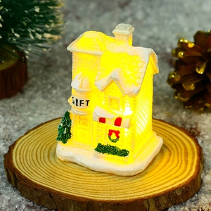 Close-up of a white resin Christmas house with warm LED light and GIFT text detail