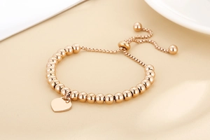 Detail of rose gold beaded bracelet featuring a heart charm and adjustable slider clasp