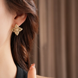Detailed view of hollow gold flower earrings with zircon inlays on a model ear